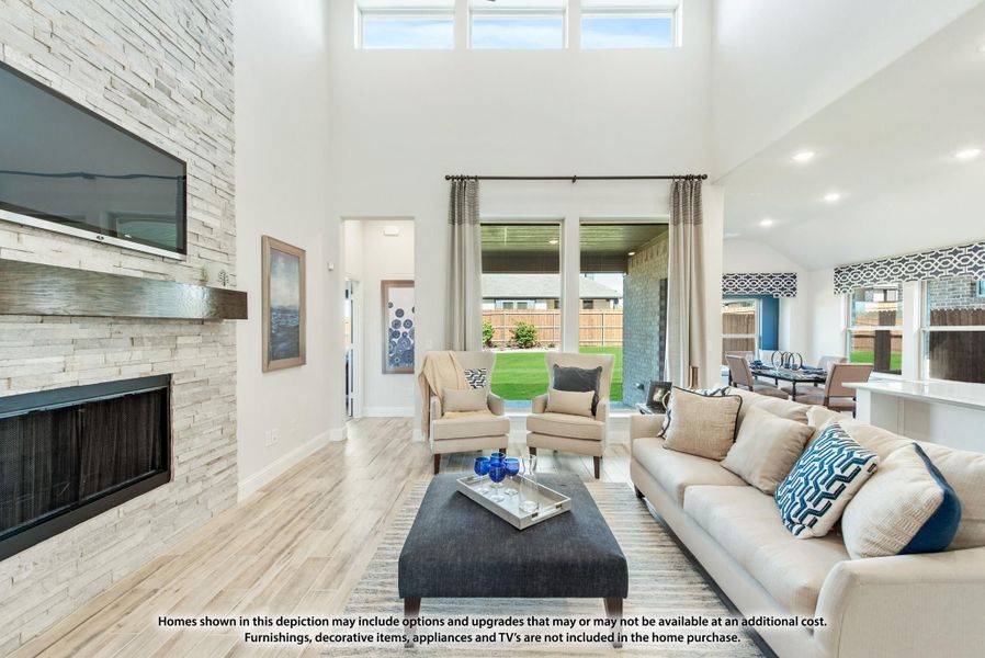 Living room with two-story ceiling, stone fireplace, wall-mounted TV, and large windows overlooking backyard