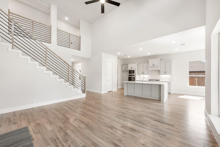 Open living area with high ceilings, wood floors, kitchen island, and staircase with metal railing
