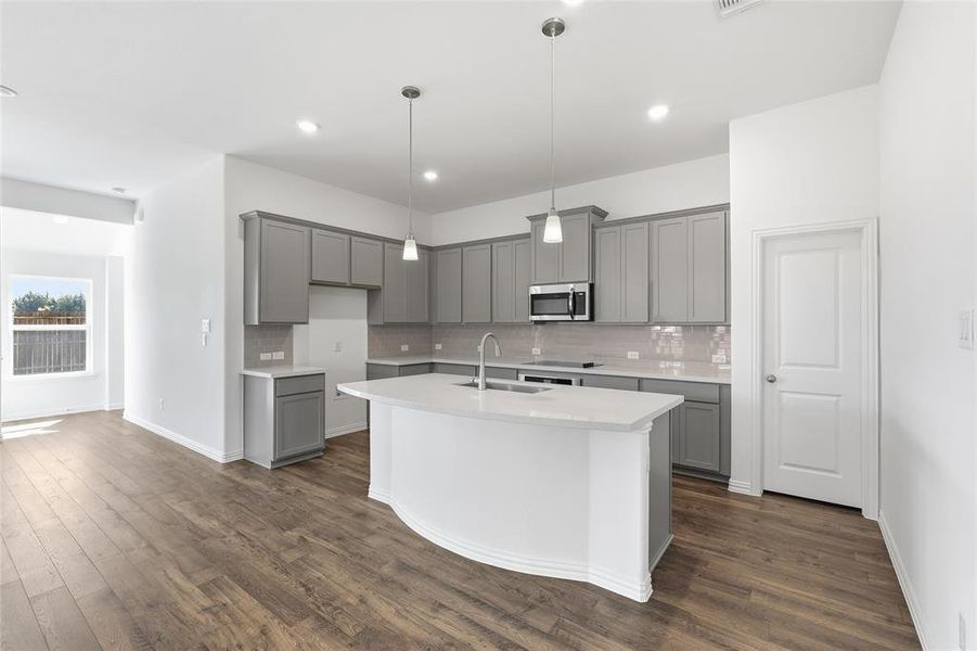Kitchen featuring an expansive island with a built-in sink, stainless steel appliances, gray shaker-style cabinetry, and wood-finish flooring