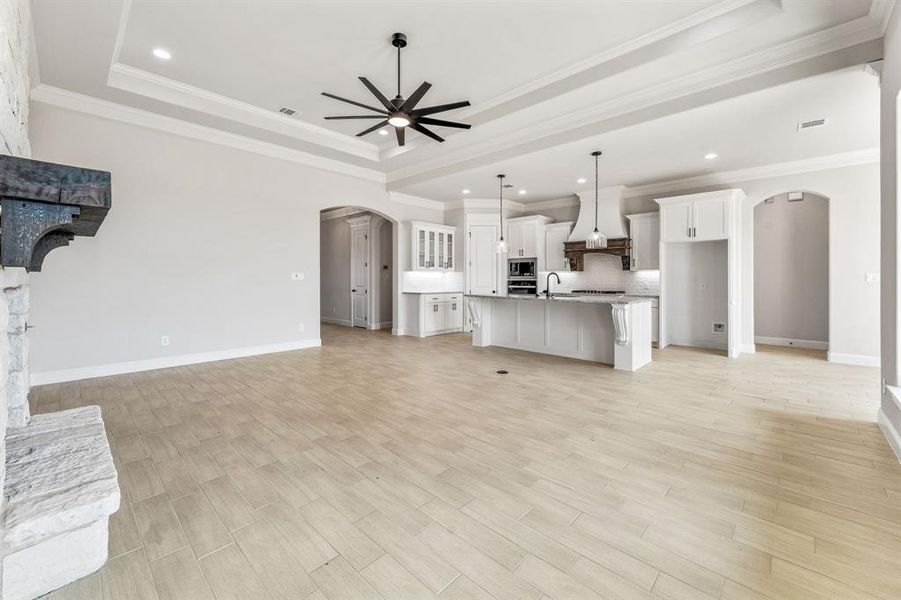 Unfurnished living room featuring arched walkways, a tray ceiling, crown molding, light wood-style floors, and ceiling fan
