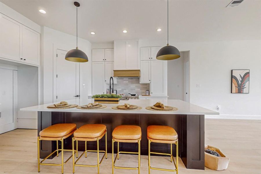 Kitchen featuring hanging light fixtures, white cabinetry, an island with sink, and light wood-type flooring