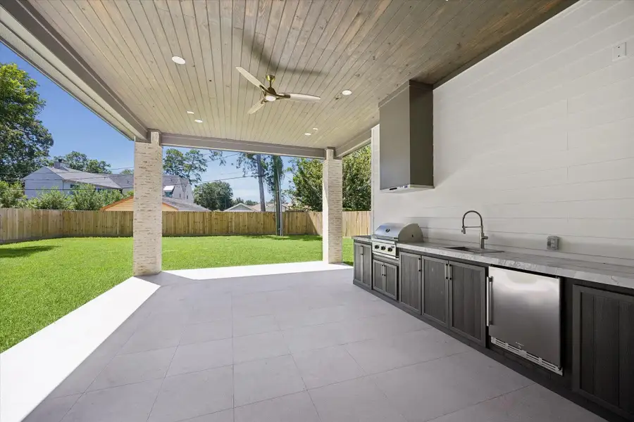The expansive covered veranda is built for year-round entertaining with a Coyote C-Series built-in gas grill, sink, beverage refrigerator, stained wood ceiling, and ample seating space overlooking the backyard.