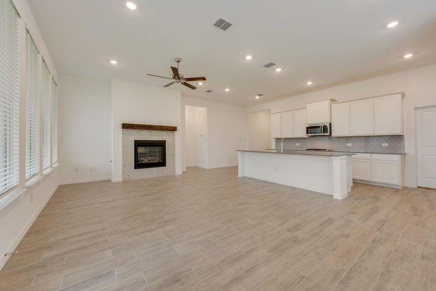 Kitchen with a fireplace, decorative backsplash, an island with sink, white cabinetry, and ceiling fan