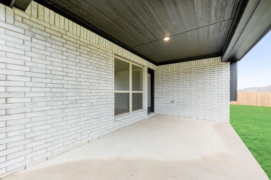 Covered back patio with concrete floor, white brick exterior, and fenced backyard with green lawn