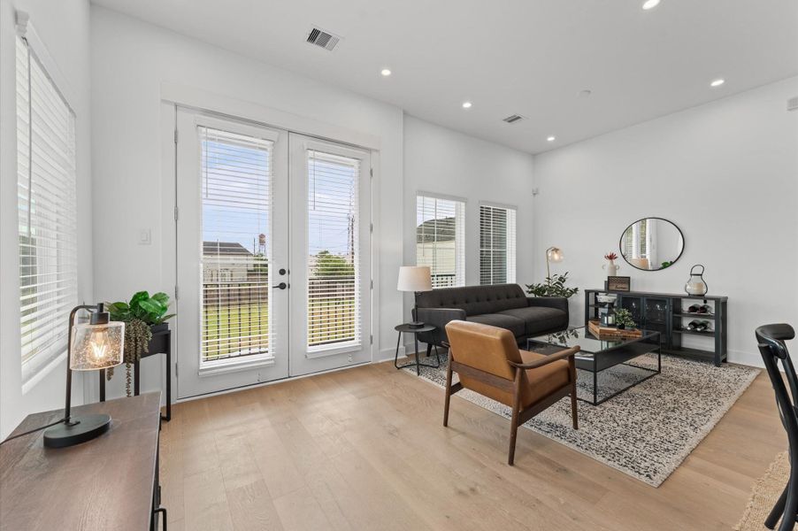 Second-story open-concept living, dining, and kitchen area bathed in natural light, featuring elegant French doors that lead to a private balcony offering a glimpse of downtown. The seamless layout offers effortless flow for entertaining, complemented by modern finishes and skyline vistas that elevate everyday living.