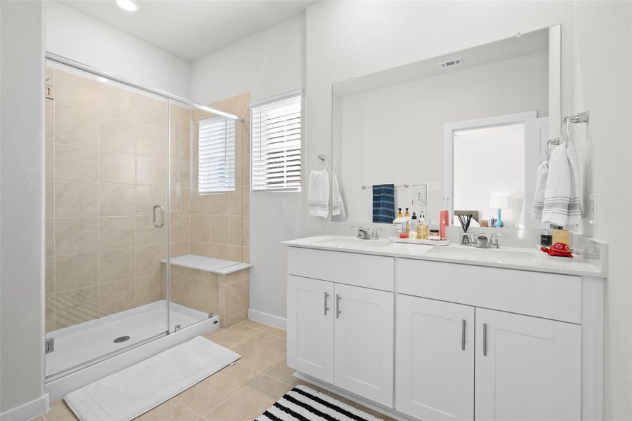 This bathroom features a spacious walk-in shower with a glass door and beige tiles. It includes a double vanity with a large mirror, white cabinetry, and modern fixtures, creating a clean and bright space.