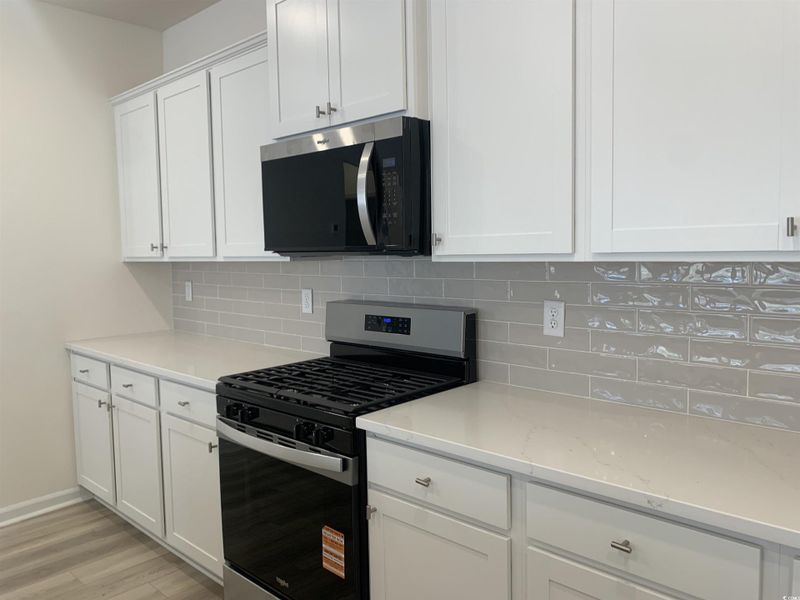 Kitchen with appliances with stainless steel finishes, white cabinets, light stone counters, light wood finished floors, and tasteful backsplash