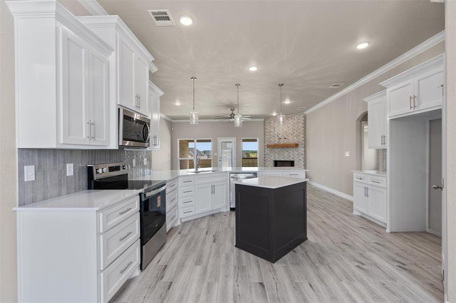 Modern kitchen featuring white cabinetry, quartz countertops, a dark-toned island, stainless steel appliances Modern kitchen featuring white cabinetry, quartz countertops, a dark-toned island, stainless steel appliances