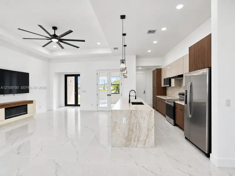Open-concept space featuring oversized stone-patterned tile flooring, a large kitchen island with stone countertop, matte black fixtures, multi-toned cabinetry, and recessed lighting