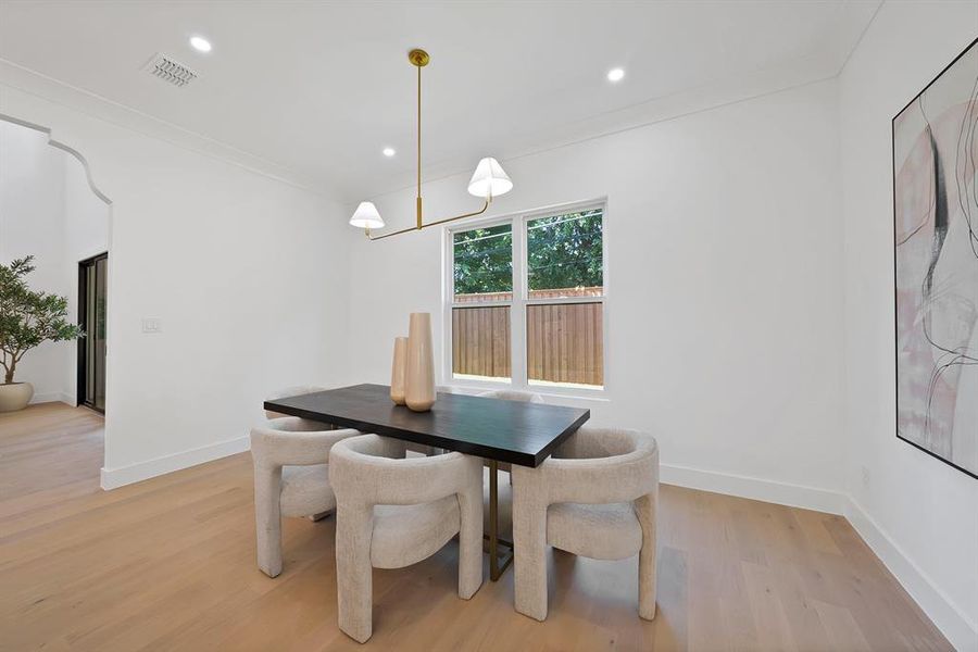 Dining space featuring light wood-finish flooring, a contemporary linear chandelier, recessed lighting, crown molding, and a single window with a privacy fence visible