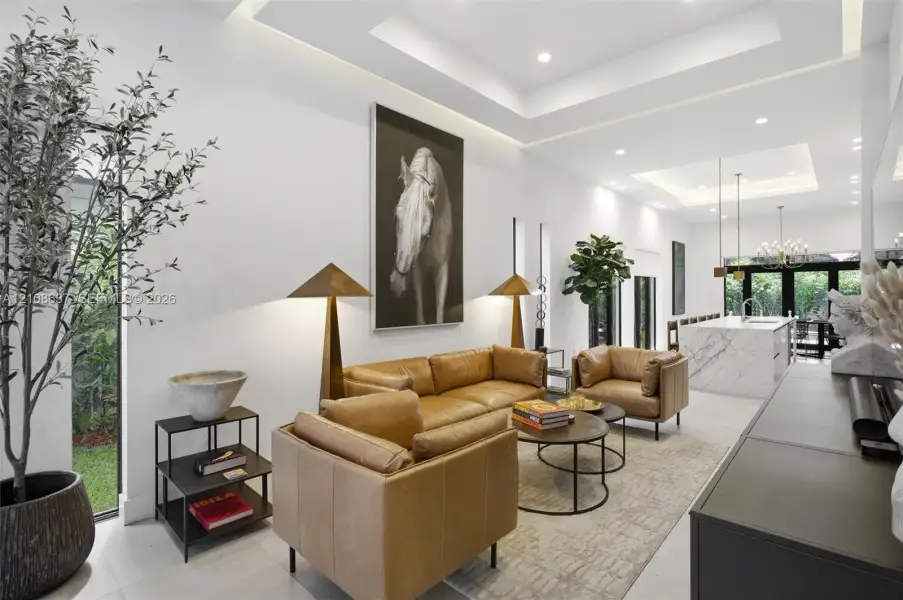 Open-concept living space featuring high ceilings with integrated tray lighting, full-height windows, recessed lighting, and a stone-clad kitchen island