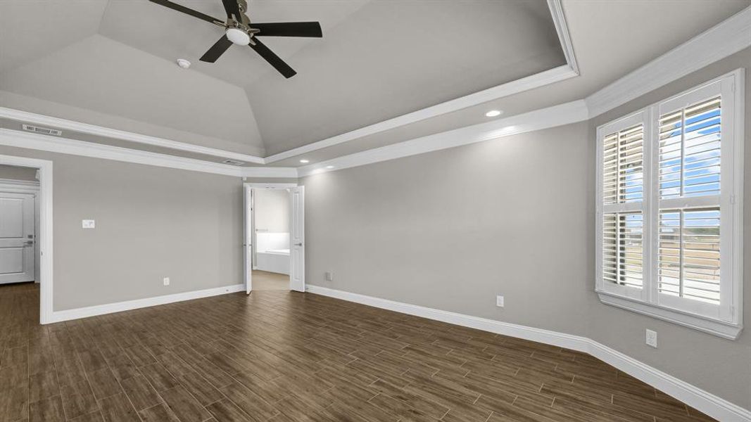 Primary Bedroom featuring crown molding, ceiling fan, dark hardwood / wood-style floors, a raised ceiling, and lofted ceiling