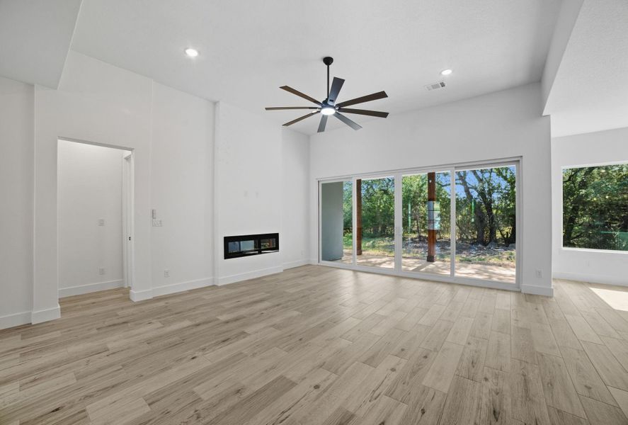 Unfurnished living room featuring a glass covered fireplace, light wood-style floors, recessed lighting, a ceiling fan, and a high ceiling Unfurnished living room featuring a glass covered fireplace, light wood-style floors, recessed lighting, a ceiling fan, and a high ceiling
