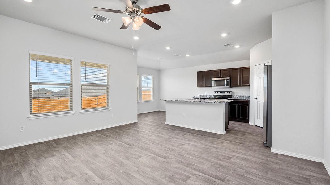 Kitchen featuring dark wood finish cabinetry, an island with sink, ceiling fan, stainless steel appliances, and open floor plan