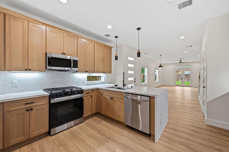 Sleek modern kitchen with stainless steel appliances, warm wood cabinetry, and elegant quartz countertops, opening up to a spacious, light-filled living area with stylish pendant lighting.