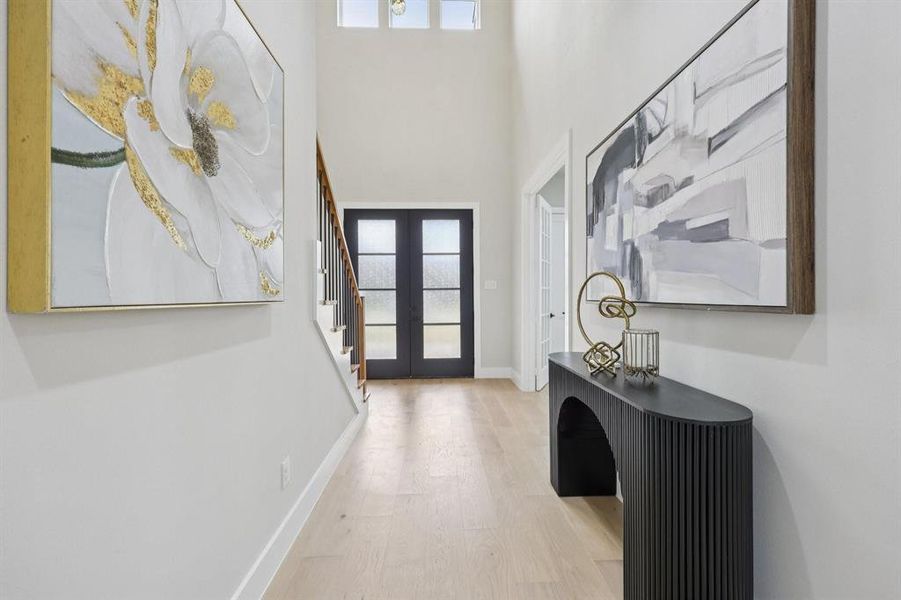 The property features a spacious entryway with light wood flooring, a staircase with dark wood handrails, and a dark-framed double door at the entrance