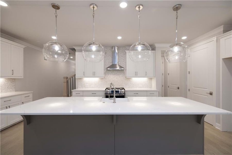 Kitchen featuring pendant lighting, a center island with sink, and wall chimney range hood