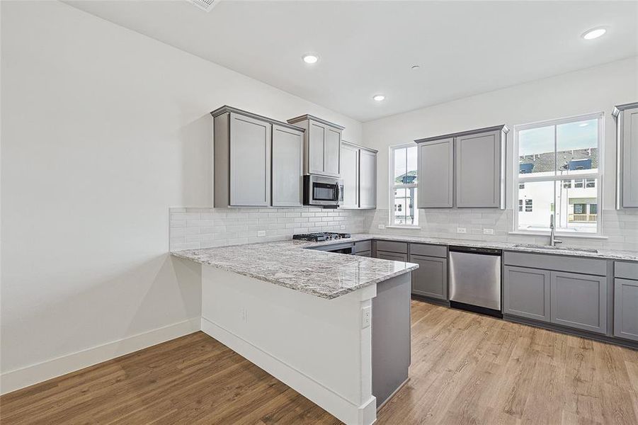 Kitchen with gray cabinetry, decorative backsplash, a peninsula, light wood-style floors, and recessed lighting
