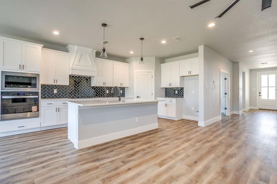 Kitchen featuring appliances with stainless steel finishes, a kitchen island with sink, white cabinetry, backsplash, and recessed lighting