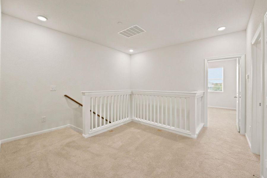 Recessed lighting illuminates a carpeted upstairs landing featuring a classic white wooden banister.