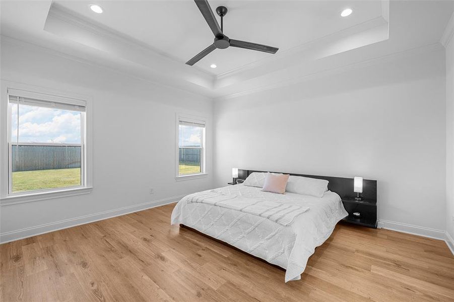 Bedroom with a tray ceiling, multiple windows, ornamental molding, and recessed lighting Bedroom with a tray ceiling, multiple windows, ornamental molding, and recessed lighting
