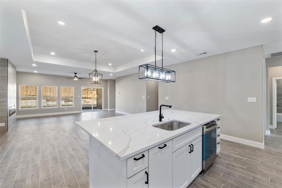 Kitchen with pendant lighting, a kitchen island with sink, sink, and white cabinets