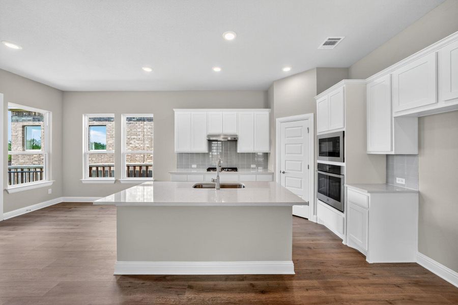 Kitchen with white cabinets, an island with sink, recessed lighting, light stone counters, and stainless steel appliances Kitchen with white cabinets, an island with sink, recessed lighting, light stone counters, and stainless steel appliances