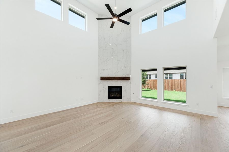 Open living room with two-story ceiling, marble fireplace, ceiling fan, and light hardwood floors Open living room with two-story ceiling, marble fireplace, ceiling fan, and light hardwood floors