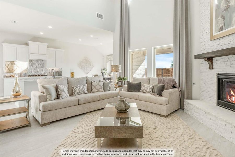 Open-concept living room with high ceilings, stone fireplace, and neutral sofas open to white kitchen