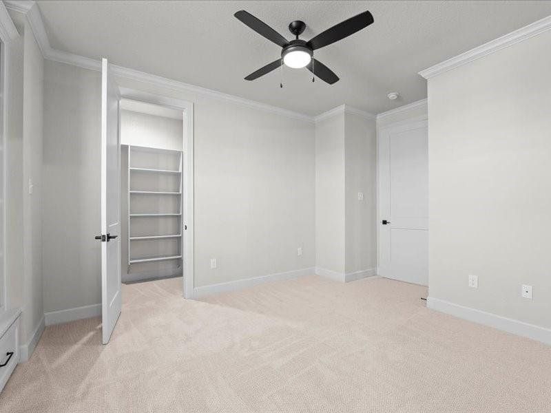 bedroom featuring a walk in closet, ornamental molding, light colored carpet, and a ceiling fan bedroom featuring a walk in closet, ornamental molding, light colored carpet, and a ceiling fan