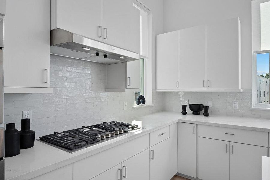 Kitchen featuring backsplash, under cabinet range hood, and white cabinets