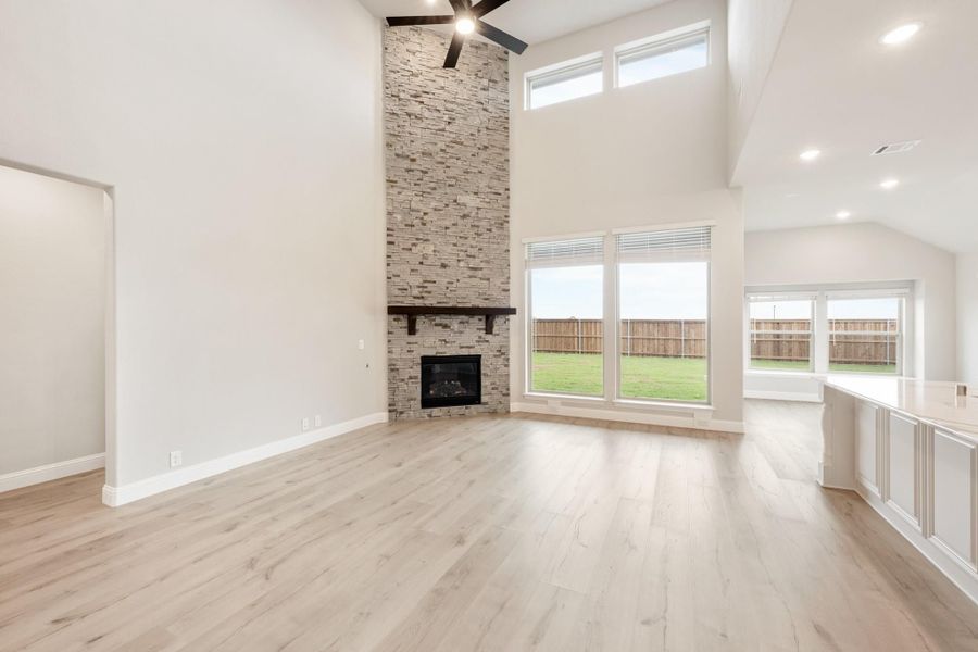 Open living room with two-story stone fireplace, light wood floors, and large windows overlooking backyard