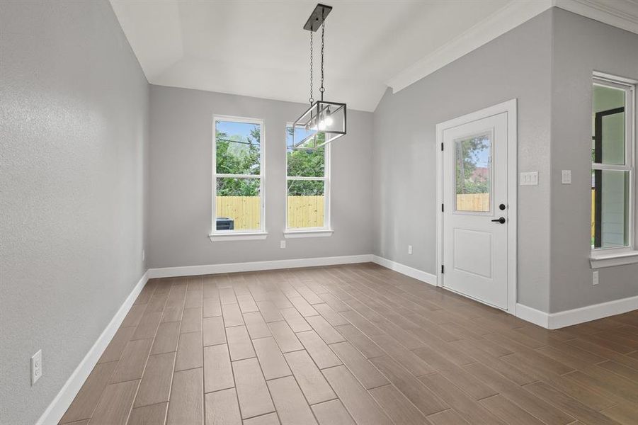 Unfurnished dining area with wood-type flooring, vaulted ceiling, ornamental molding, and a notable chandelier