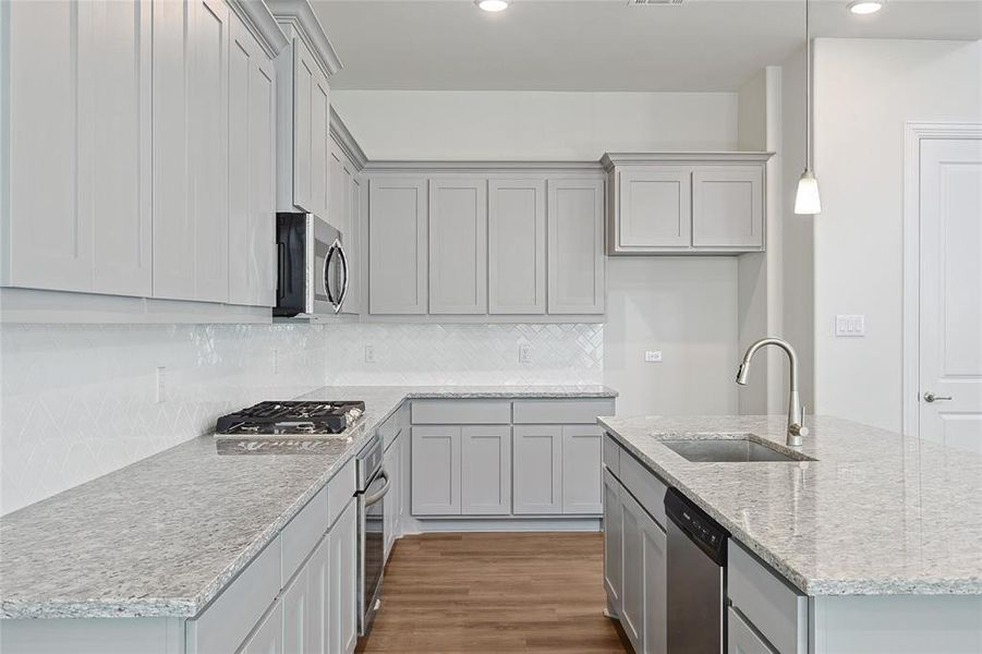 Kitchen with an island with sink, dark wood-style floors, light stone countertops, stainless steel appliances, and backsplash Kitchen with an island with sink, dark wood-style floors, light stone countertops, stainless steel appliances, and backsplash