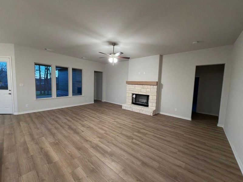 Unfurnished living room with wood finished floors, ceiling fan, and a stone fireplace