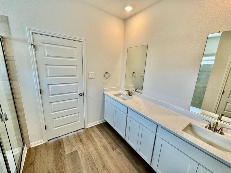 Bathroom featuring light wood-type flooring, double vanity, a shower with shower door, and a textured wall