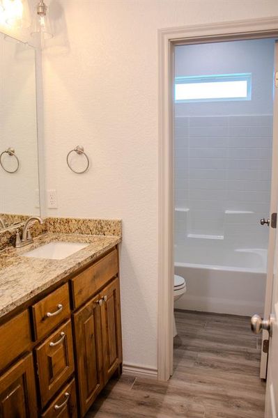 Full bath featuring vanity, wood finished floors, a textured wall, and bathing tub / shower combination Full bath featuring vanity, wood finished floors, a textured wall, and bathing tub / shower combination