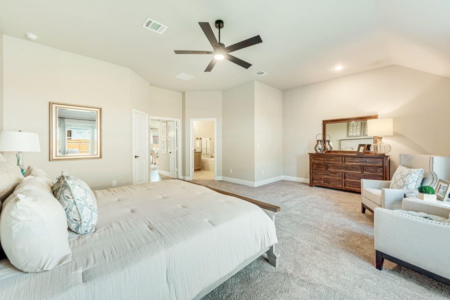 Spacious master bedroom with vaulted ceiling, ceiling fan, carpet floors, and ensuite bathroom access
