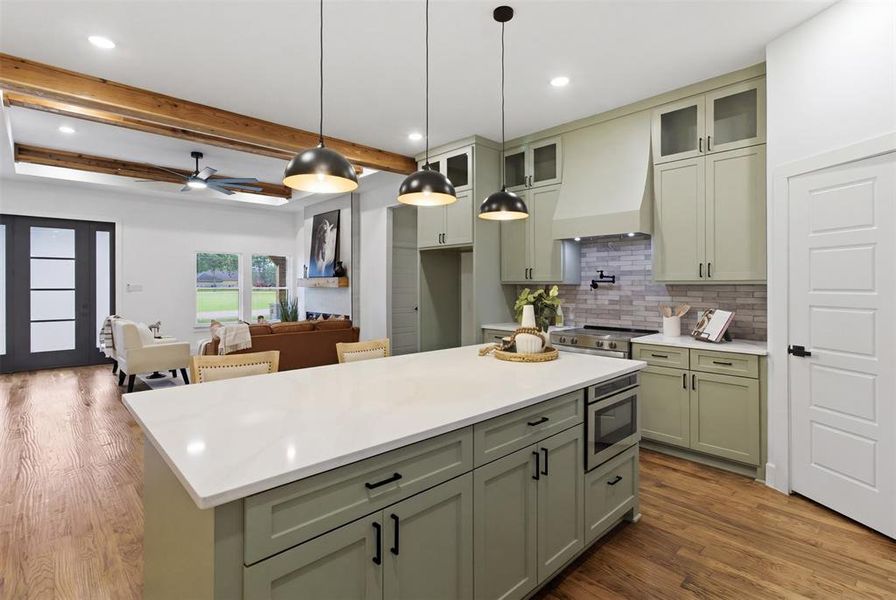 Open-concept kitchen featuring an oversized island with white countertop, sage green cabinetry with black hardware, and pendant lighting