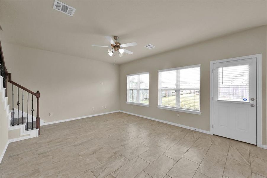 This is a spacious, well-lit room featuring tiled flooring, a ceiling fan, and multiple windows that provide ample natural light.