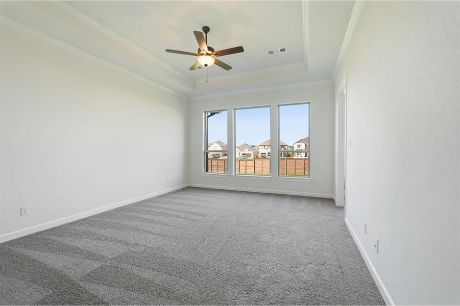 Spacious room featuring a tray ceiling with crown molding, a ceiling fan with integrated lighting, and plush gray carpeting