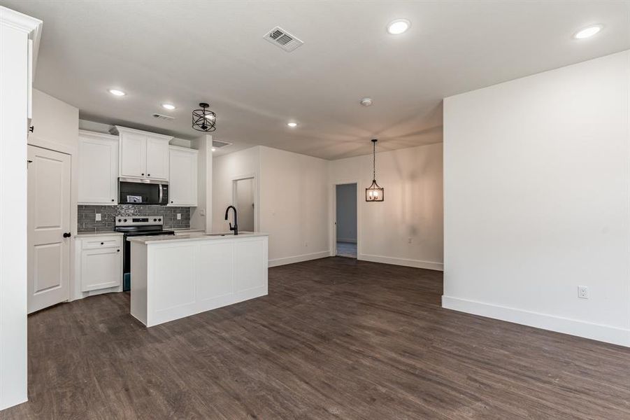 Kitchen with dark wood-type flooring, white cabinetry, an island with sink, stainless steel appliances, and backsplash