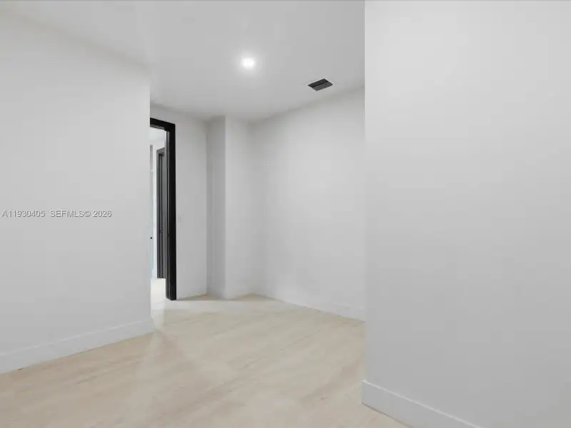 Interior space featuring light-toned wood-finish flooring, crisp white walls, recessed ceiling lighting, and a dark-framed doorway Interior space featuring light-toned wood-finish flooring, crisp white walls, recessed ceiling lighting, and a dark-framed doorway