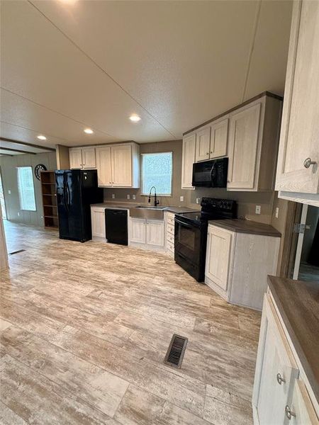Kitchen with black appliances, dark countertops, light wood-style floors, plenty of natural light, and recessed lighting