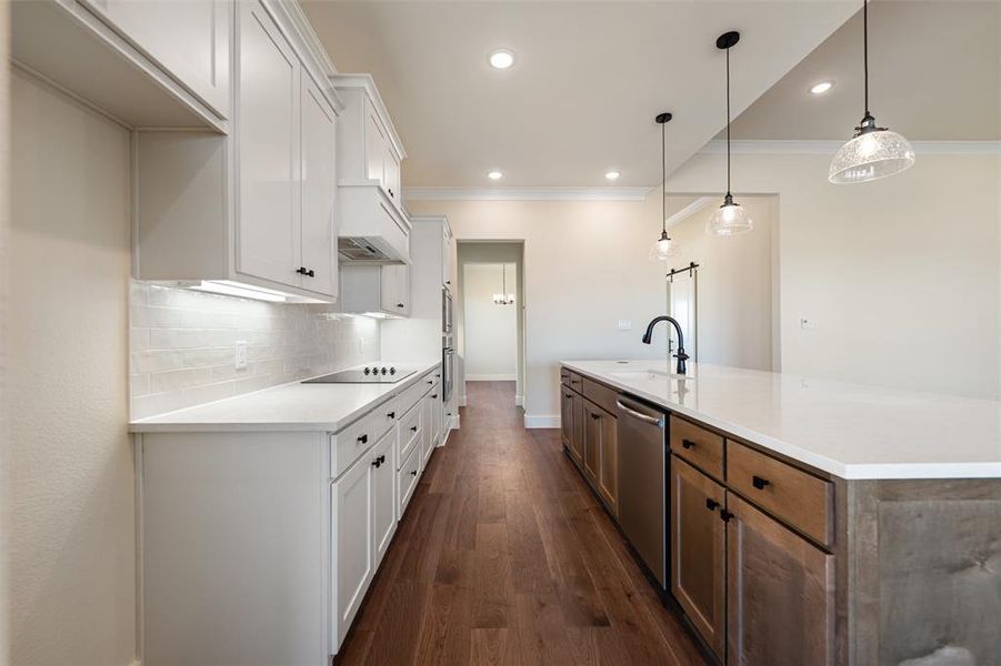 Kitchen with white cabinets, backsplash, a center island with sink, decorative light fixtures, and dark wood finished floors