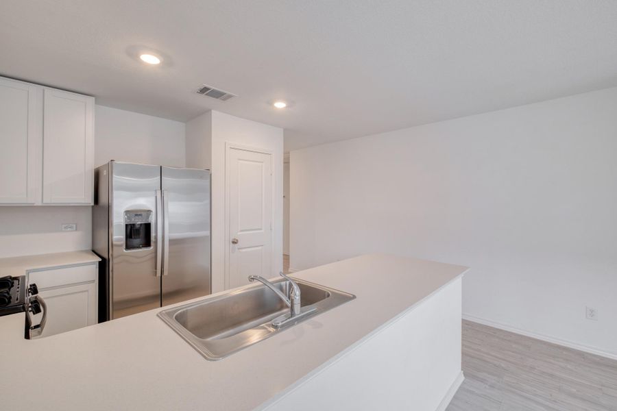 Modern kitchen featuring a stainless steel refrigerator, white cabinetry, integrated sink, and recessed lighting