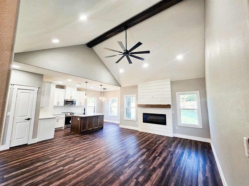 Living room view w/ electric fireplace, custom wood mantle, vaulted ceiling, and 
luxury vinyl flooring.