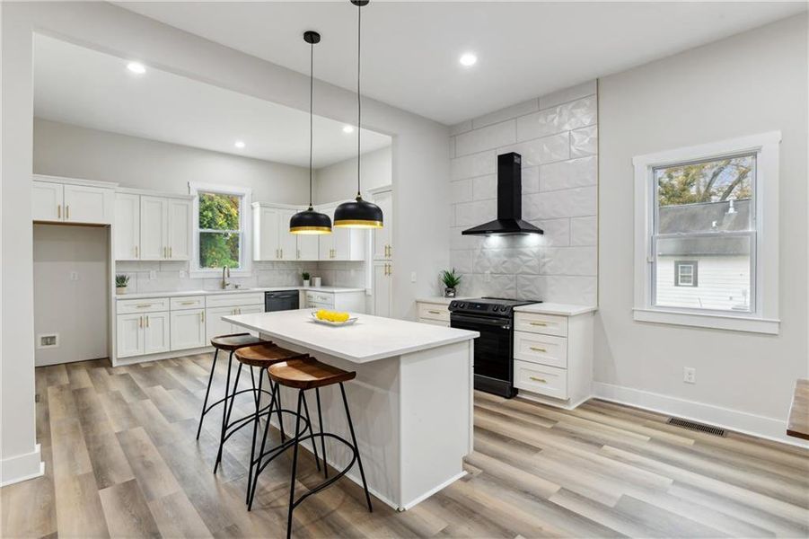 Kitchen with tasteful backsplash, white cabinets, black appliances, and wall chimney exhaust hood