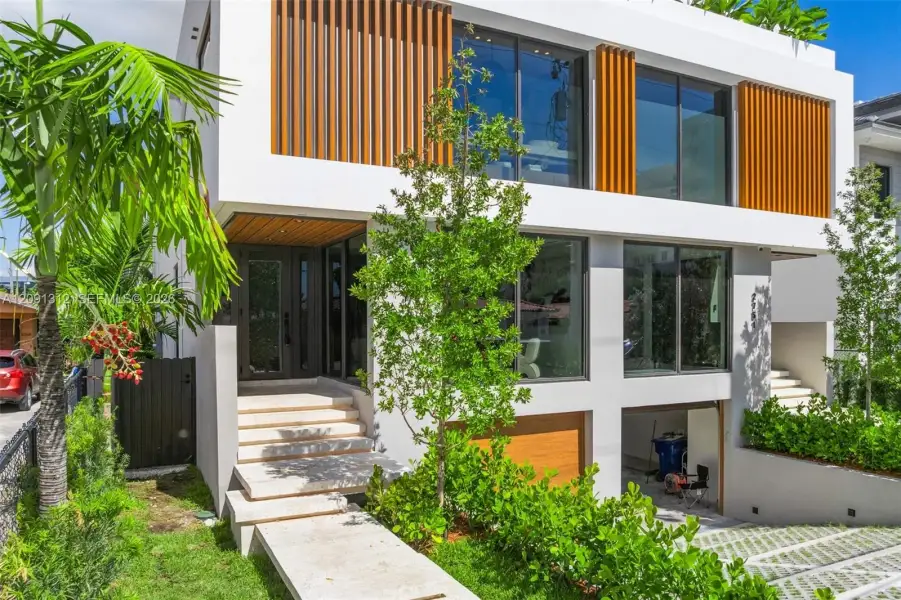 Contemporary exterior featuring clean-lined white stucco, vertical wood-finish louvers, expansive floor-to-ceiling windows, a stone-paved entry staircase, and a tiered driveway with permeable pavers Contemporary exterior featuring clean-lined white stucco, vertical wood-finish louvers, expansive floor-to-ceiling windows, a stone-paved entry staircase, and a tiered driveway with permeable pavers