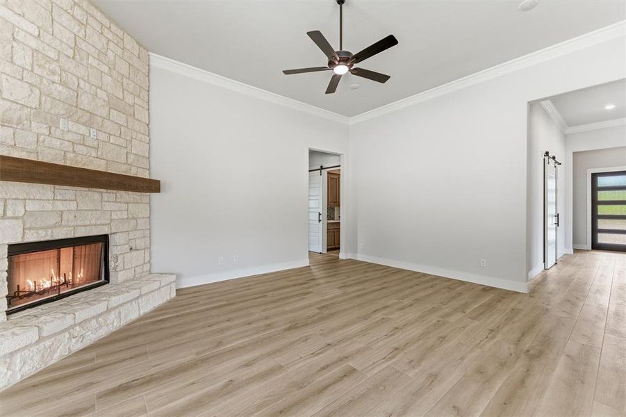 Unfurnished living room with a barn door, crown molding, light wood-style flooring, and a ceiling fan
